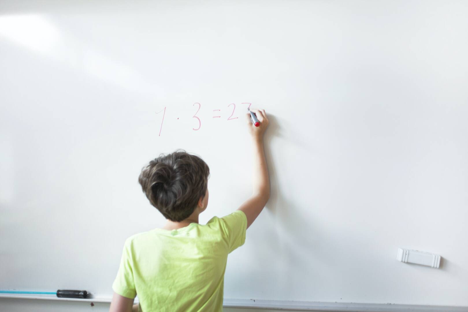 Rear view of schoolboy solving mathematics on whiteboard in classroom